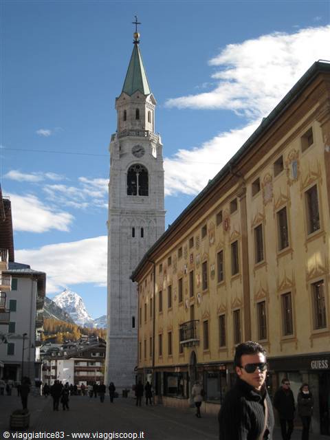 White bell tower of Cortina d'Ampezzo between painted buildings and pedestrians