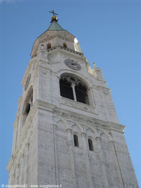 White stone bell tower with clock and green spire against blue sky