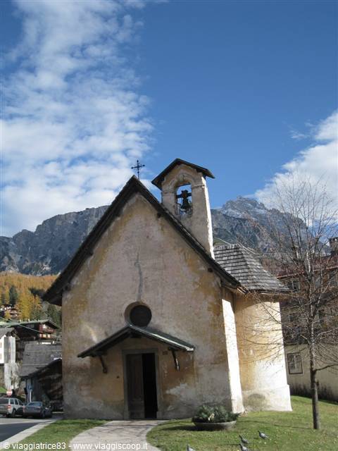 Small stone church with bell tower beneath snowy Dolomites in Cortina