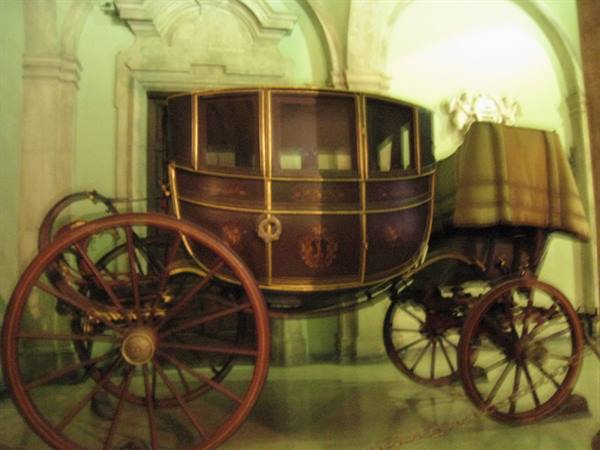 Antique wooden and gilded carriage displayed in a stone-arched hall