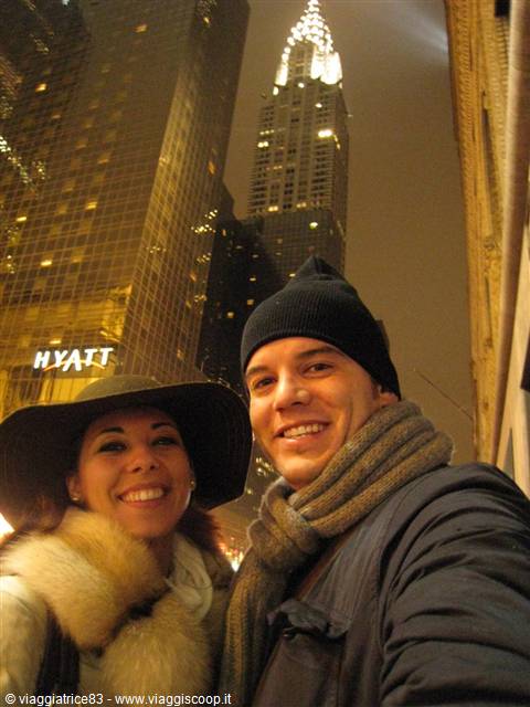 Couple selfie in winter coats beneath the illuminated Chrysler Building at night