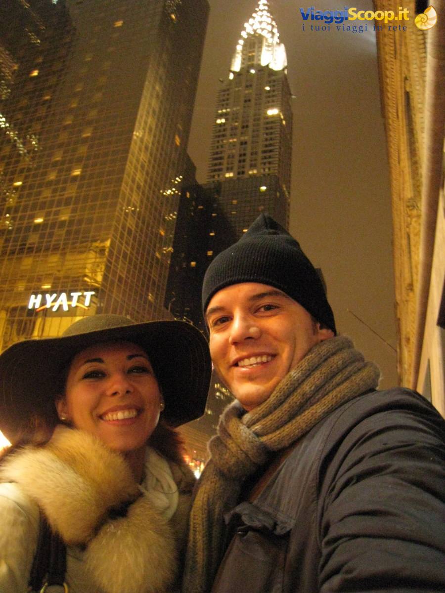 Couple selfie in winter coats beneath the illuminated Chrysler Building at night