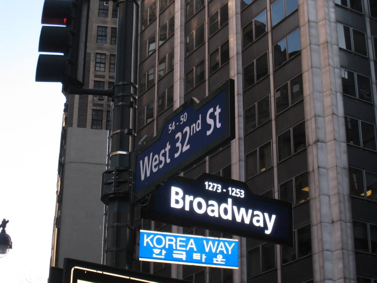 Street signs for Broadway and West 32nd St in front of skyscraper