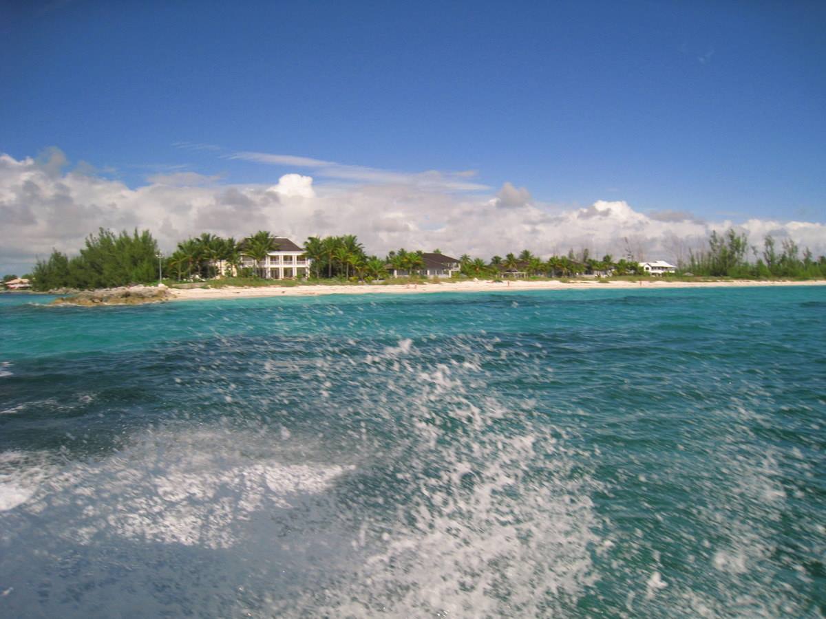 Boat wake on turquoise water near beach with villas and palms