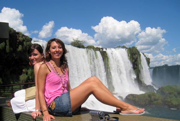 Two smiling tourists posing in front of Iguazu Falls on a sunny day