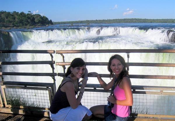 Two smiling tourists on the metal walkway in front of Iguazú Falls