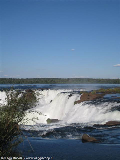 Iguazu Falls, foaming water cascades over basalt rocks under blue sky