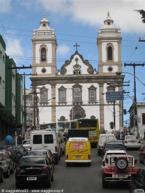 Baroque colonial church with twin towers, buses and a yellow van in traffic
