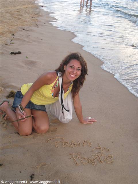 Woman in yellow writes Praia do Forte on wet sand, waves behind her