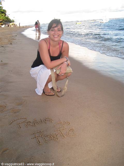 Woman crouching on the sand at Praia do Forte, next to a message written in sand