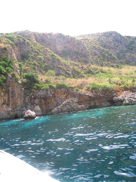 Rocky cliffs with Mediterranean scrub above turquoise water, photographed from a boat