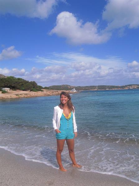 Smiling woman in turquoise romper and white jacket on the foamy shoreline