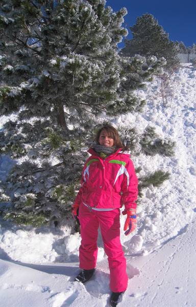Woman in pink ski suit beside a snow-covered pine tree under sunny sky