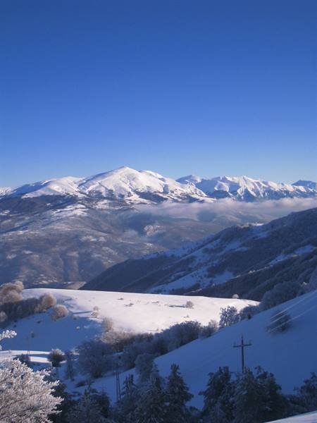 Snow-capped peaks and low fog over white hills and frosted trees