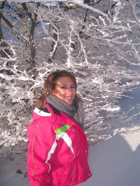 Smiling woman in pink jacket and gray scarf among snow-covered trees