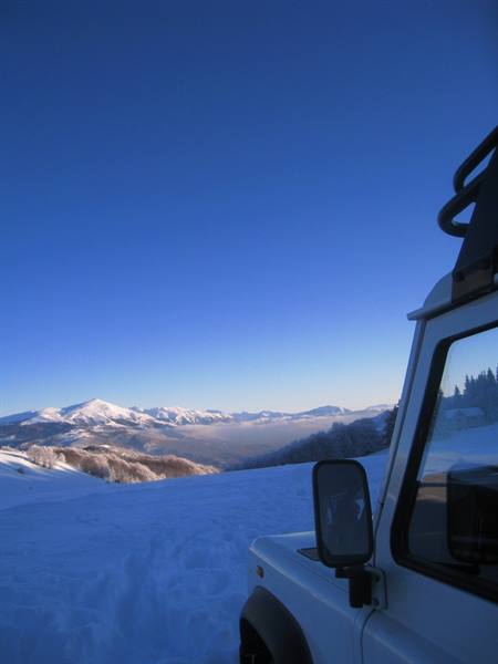 White 4x4 parked on snow facing snowy mountains under a deep blue sky