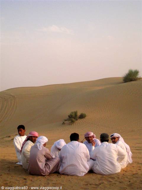 Men in white robes sitting in a circle on the sand among dunes