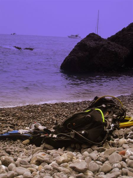Scuba gear on pebbles, a boat beyond dark rocks