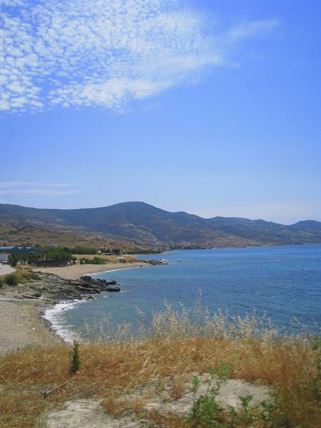 Sandy beach with rocks washed by blue sea, dry hills in the background