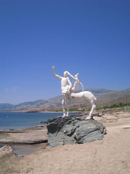 White centaur statue on grey rock, sandy beach and blue sea