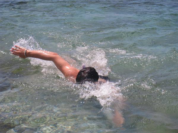 Woman swims crawl in clear green sea, arm raised amid splashes