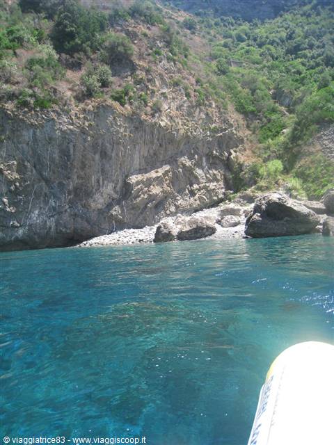 Boat bow over clear turquoise water near rocky cliffs and pebble shore