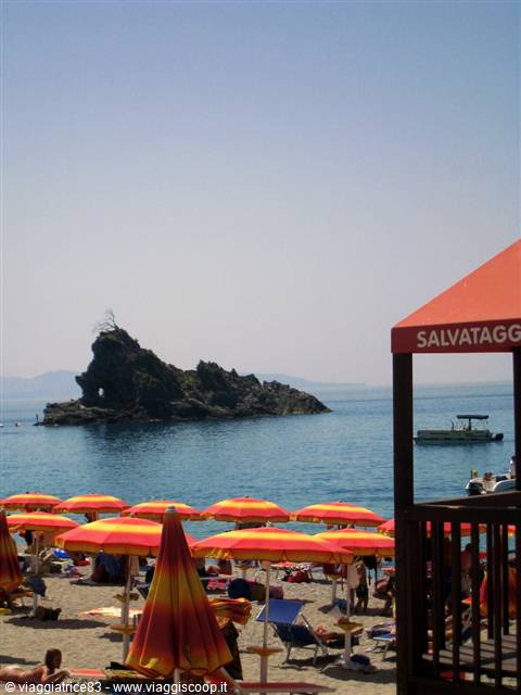 Beach with red and yellow umbrellas, rocky outcrop on blue sea