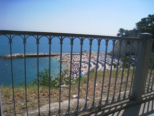Iron railing in front of crowded Pugnochiuso beach, umbrellas and white cliff