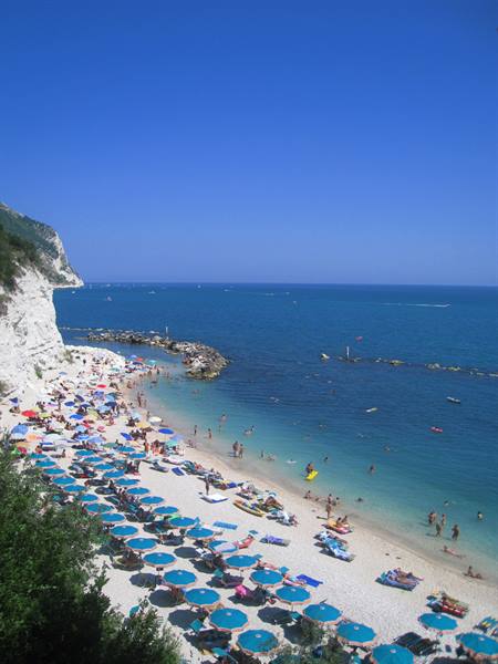 Beach with blue umbrellas beneath white limestone cliffs, swimmers in clear water