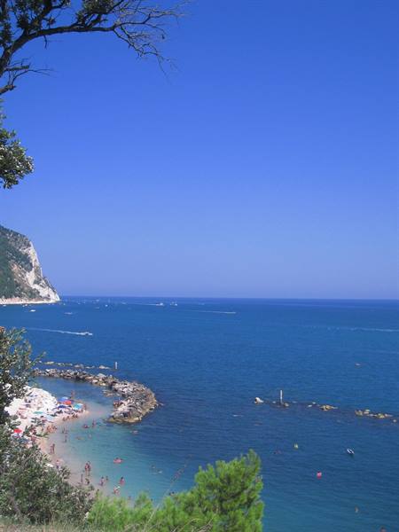 Beach with umbrellas and rocky breakwater beneath the Conero cliff