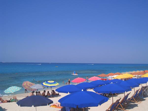 Beach with blue and colorful umbrellas, people sunbathing, turquoise sea and clear sky