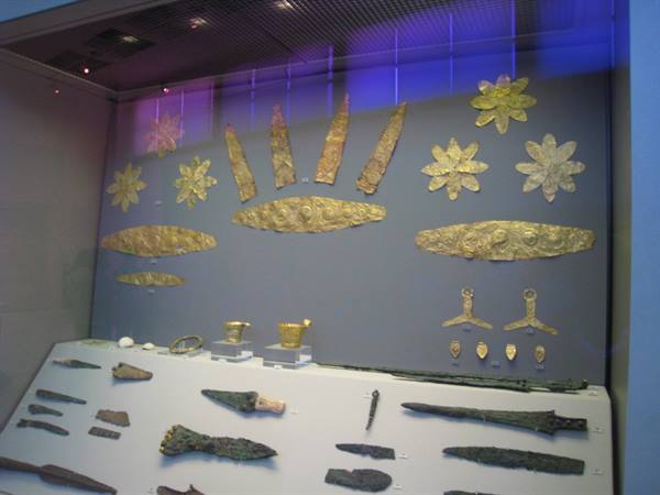 Ancient blades and gold ornaments displayed in museum case under blue light