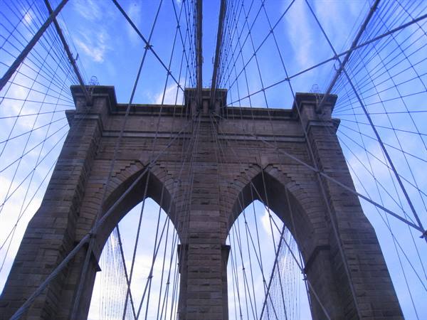 Granite tower of the Brooklyn Bridge with steel cables against blue sky