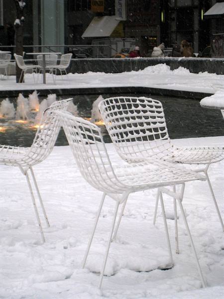 White wire chairs covered in snow beside a lit fountain