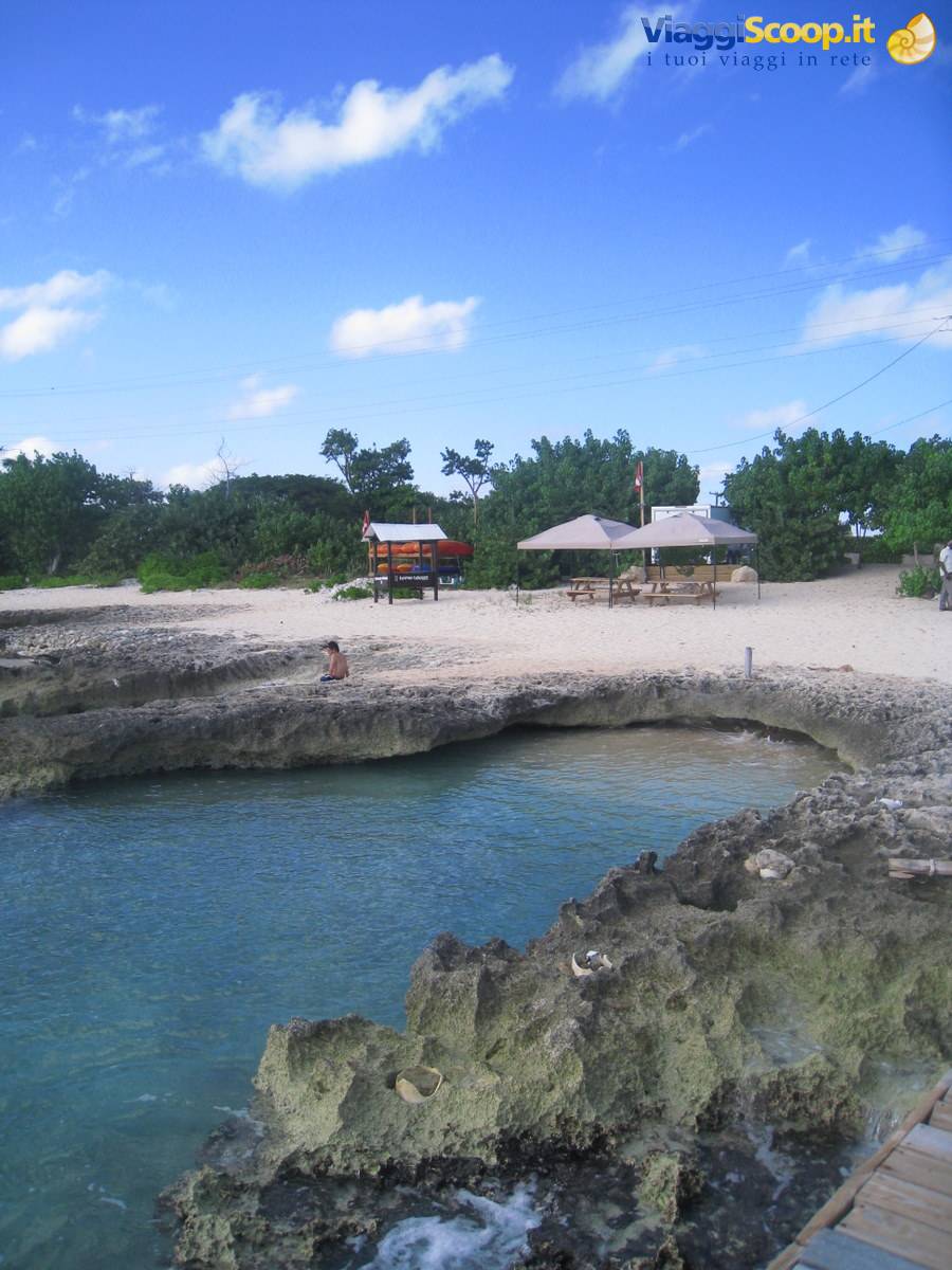 Sandy beach with umbrellas and tables among coral rocks and turquoise water