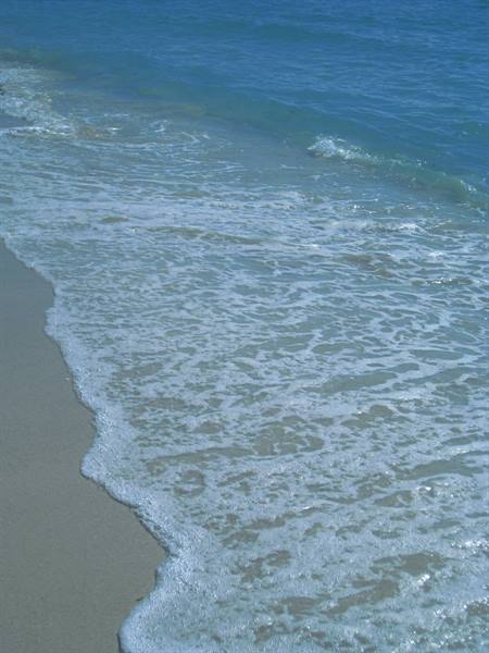 White foamy wave washing over pale sand, deep blue sea