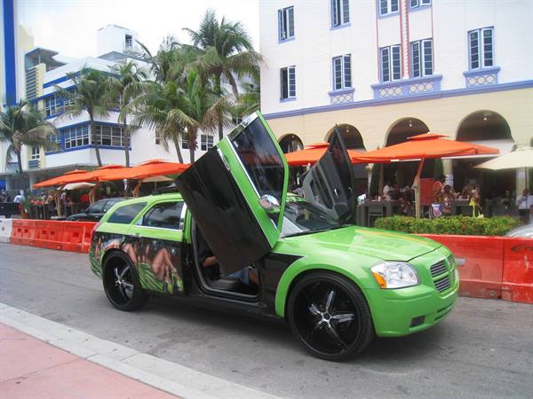 Green car with gullwing doors on Ocean Drive, orange umbrellas and palms
