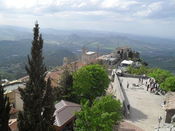 Tourists on the stone square of San Marino among lime trees and tiled rooftops