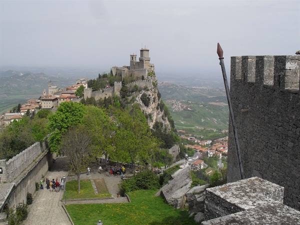Visitors on green path below San Marino's First Tower atop rocky cliff