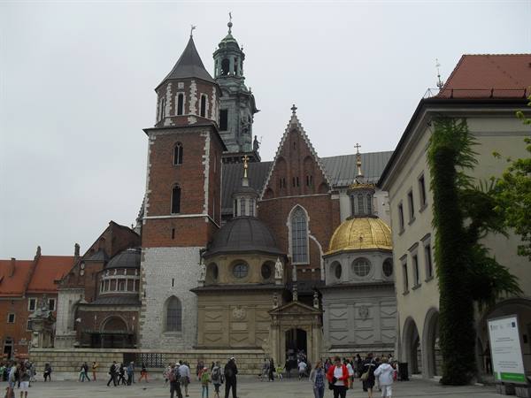 Tourists walk in front of Wawel Cathedral in Kraków, golden dome under grey sky