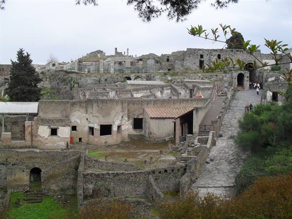 Tourists walk among the ancient stone ruins of Herculaneum under a grey sky
