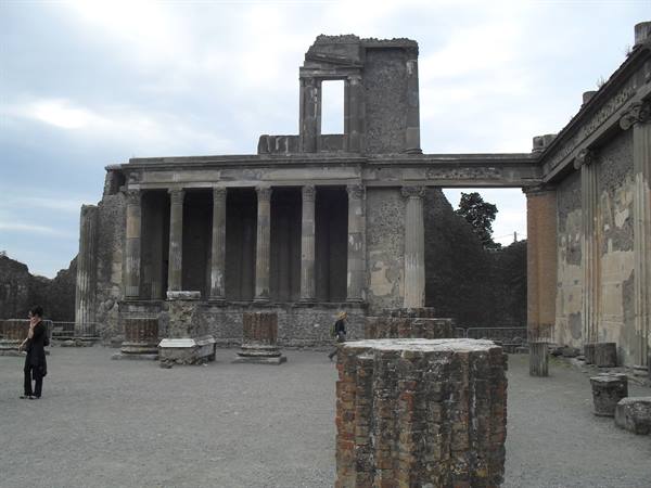 Stone column ruins at Pompeii under cloudy sky, visitors walking by