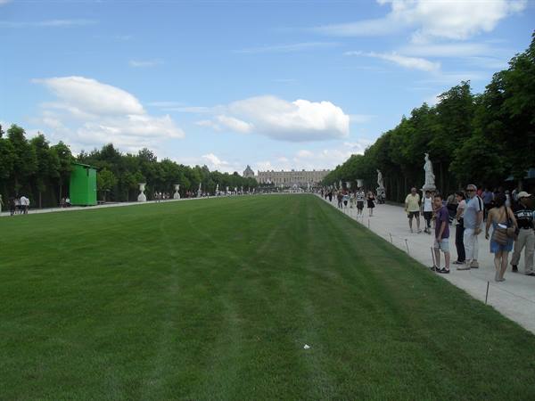 Tourists strolling along the Versailles gardens avenue between lawn and statues