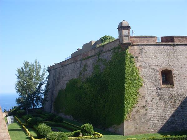 Ivy-covered stone walls of Montjuïc Castle with gardens and sea below
