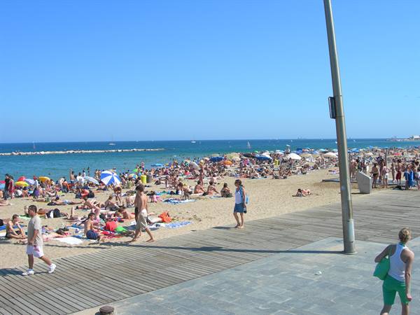 Crowded beach with colorful umbrellas, wooden boardwalk and blue sea