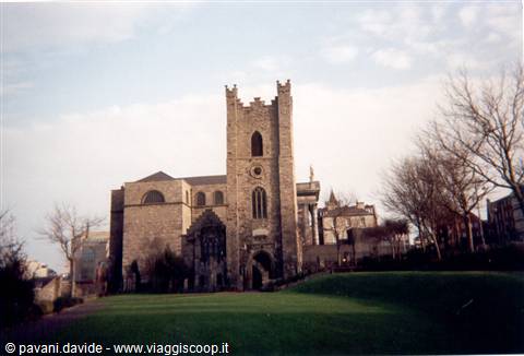 Medieval stone church with bell tower, green lawn and bare trees in front