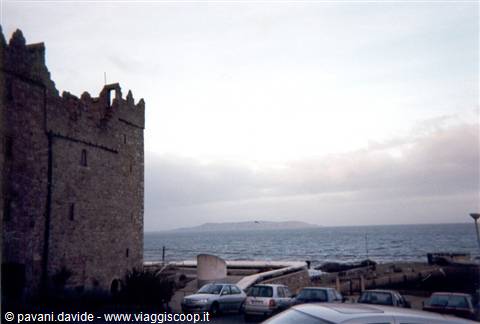 Old stone tower by the sea, parked cars, cloudy sky