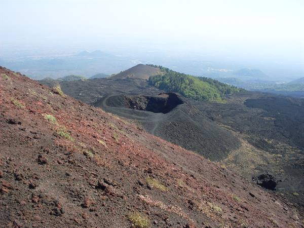 Extinct volcanic crater surrounded by black lava and red scoria, Mount Etna