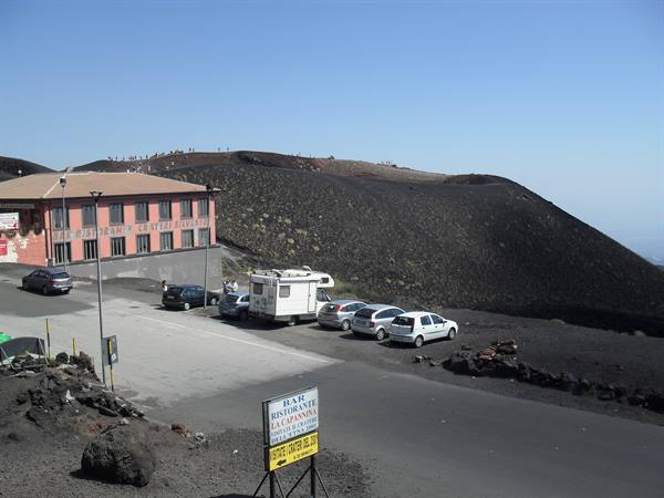 Camper and cars parked beside pink building on black lava at Mount Etna