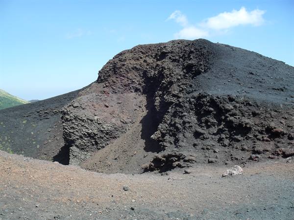 Volcanic cinder cone of black and red lava under blue sky, sandy slopes